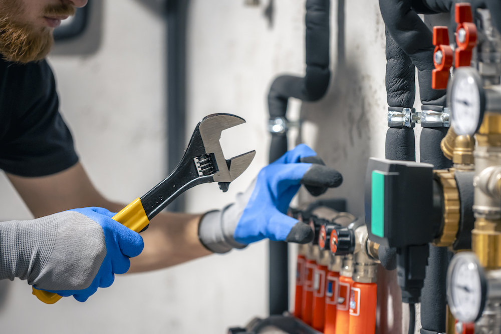 A man installs a heating system in a house and checks the pipes with a wrench.